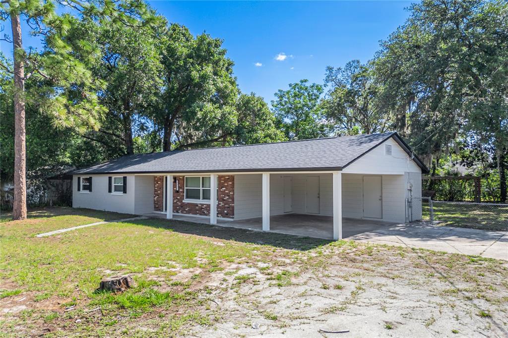 A single-story house with a carport, brick accents, and a gray roof under large trees — 2201 CAMELLIA DRIVE, LONGWOOD, FL