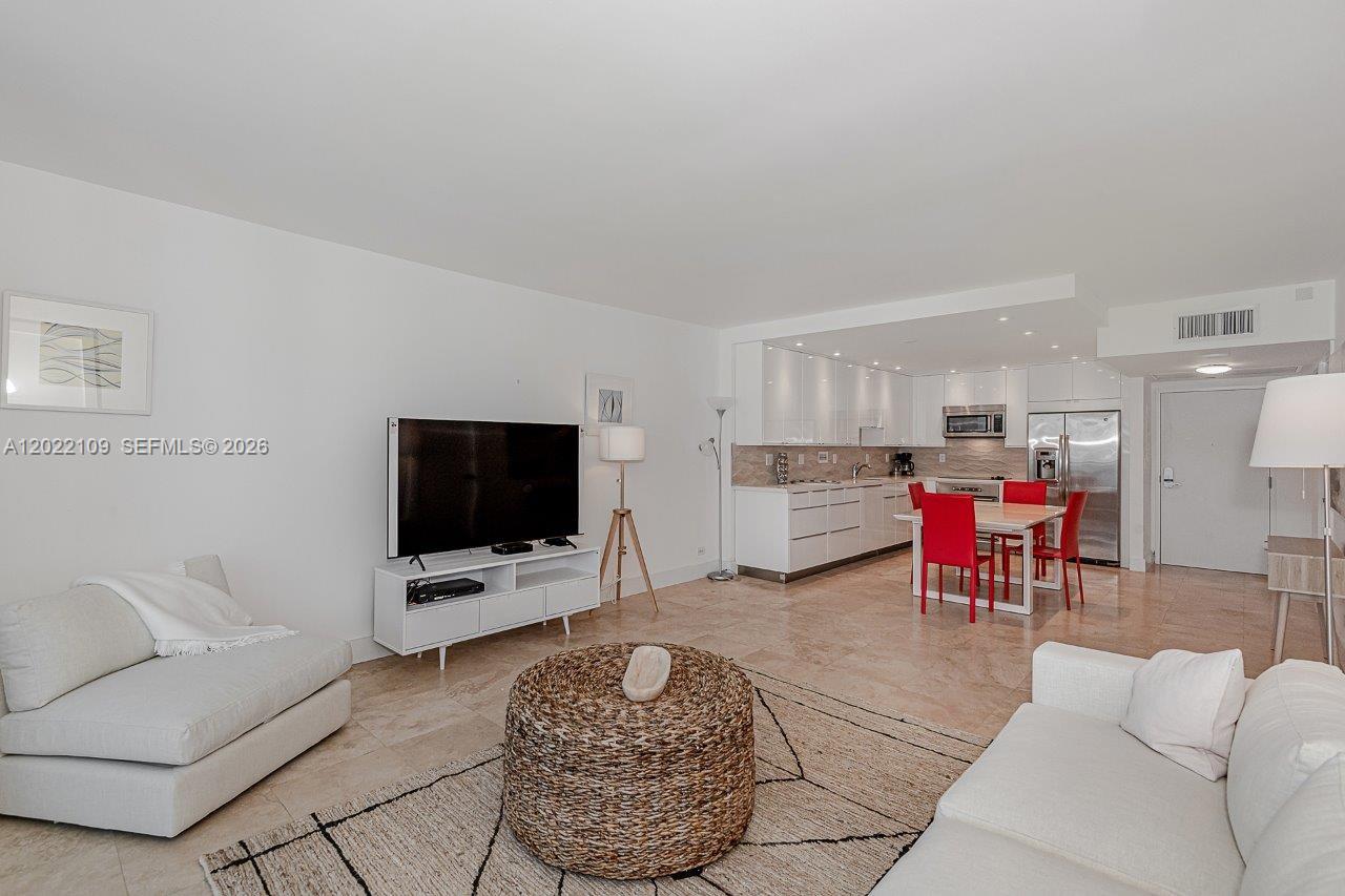 An open-concept living and dining area features white cabinetry, tile flooring, and red chairs — 2301 Collins Ave # 1515, Miami Beach FL 33139, MIAMI BEACH, FL