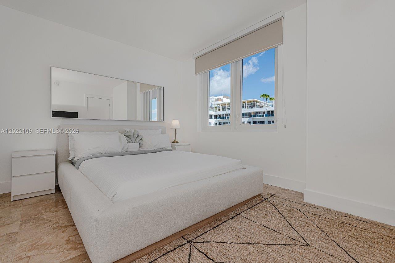 A modern bedroom features a white platform bed, a large wall mirror, and a window — 2301 Collins Ave # 1515, Miami Beach FL 33139, MIAMI BEACH, FL