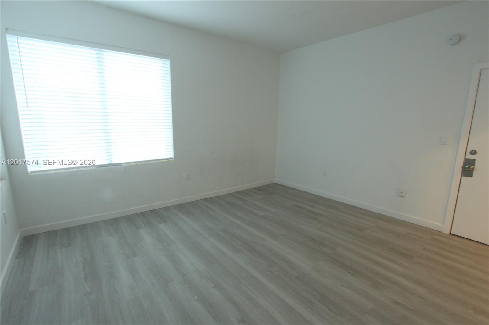 An empty room features white walls, light wood-look flooring, and a window with blinds — 1115 Euclid Ave # 17, Miami Beach FL 33139, MIAMI BEACH, FL