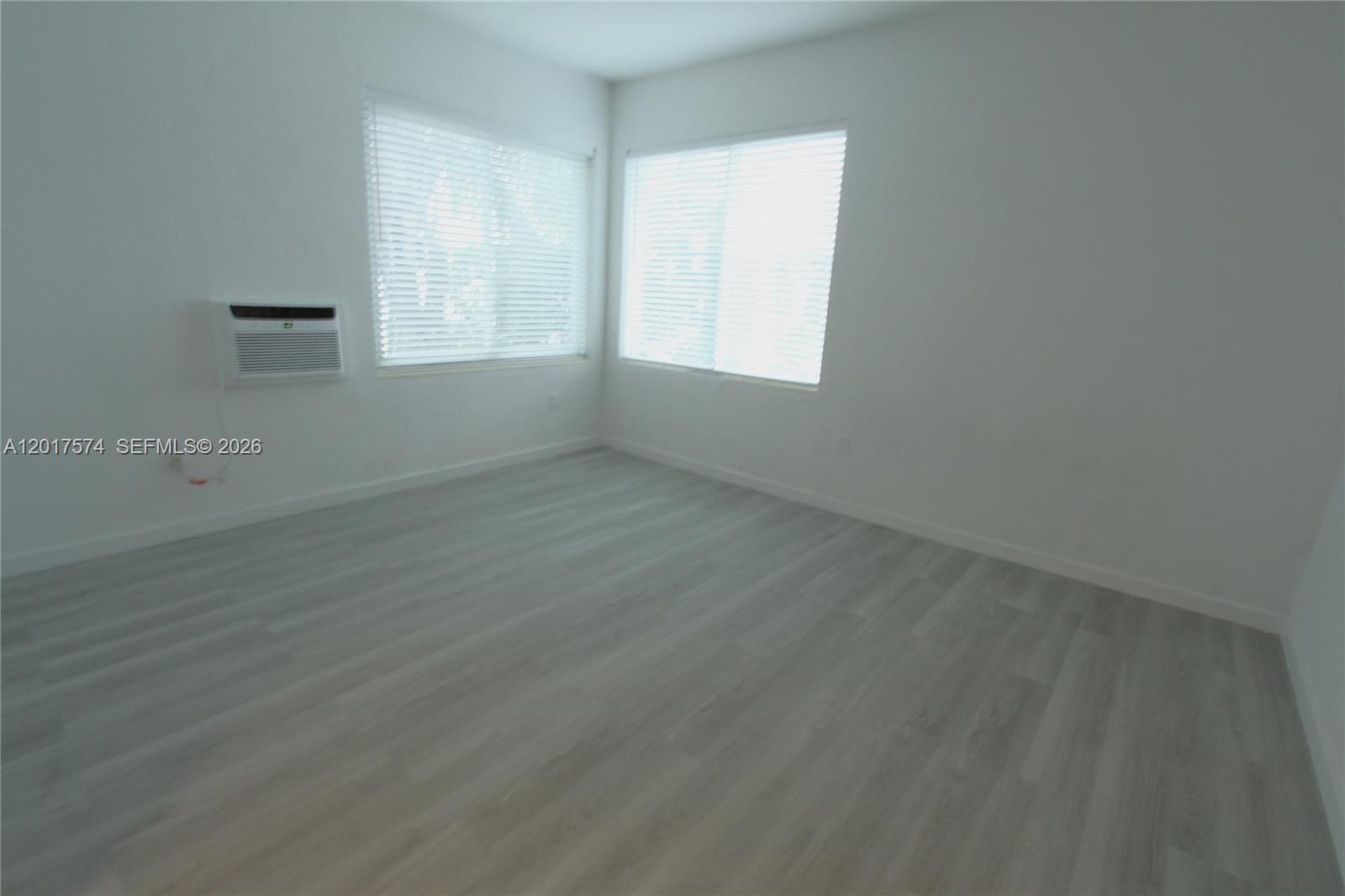 An empty room features white walls, light wood-look flooring, two windows, and a wall-mounted air conditioner — 1115 Euclid Ave # 17, Miami Beach FL 33139, MIAMI BEACH, FL
