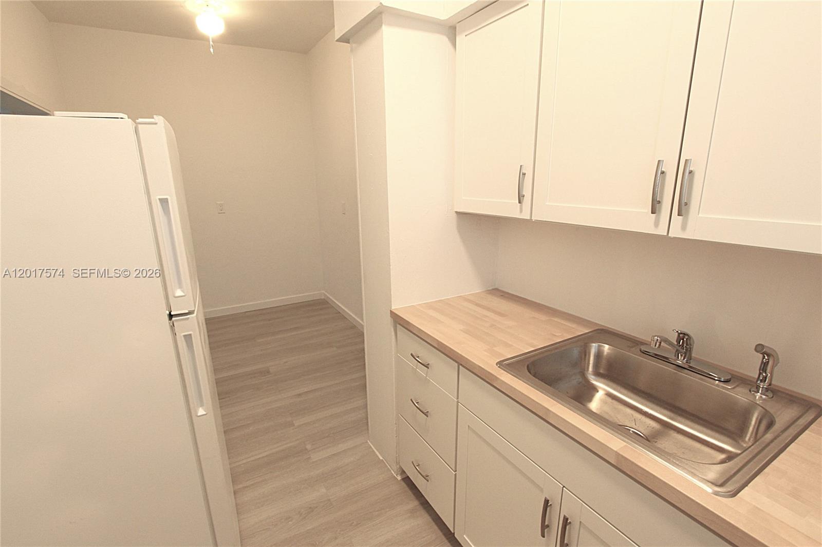 A kitchen features white cabinets, a stainless steel sink, wood-look countertops, and a white refrigerator — 1115 Euclid Ave # 17, Miami Beach FL 33139, MIAMI BEACH, FL