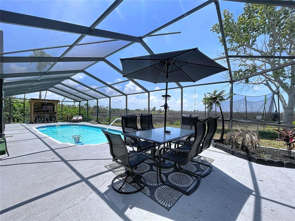 A screened-in patio features a dining set, a swimming pool, and a tiki bar — 6950 SOUTHWIND DRIVE, HUDSON, FL