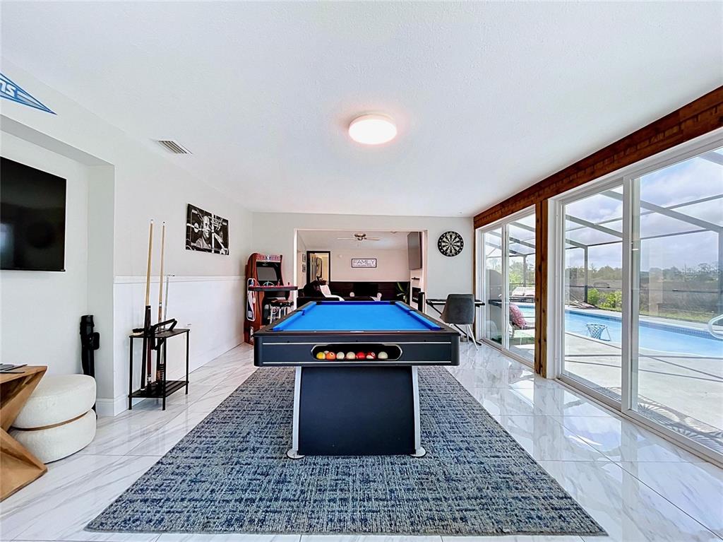 A game room features a pool table, tiled floors, and sliding glass doors overlooking a pool — 6950 SOUTHWIND DRIVE, HUDSON, FL