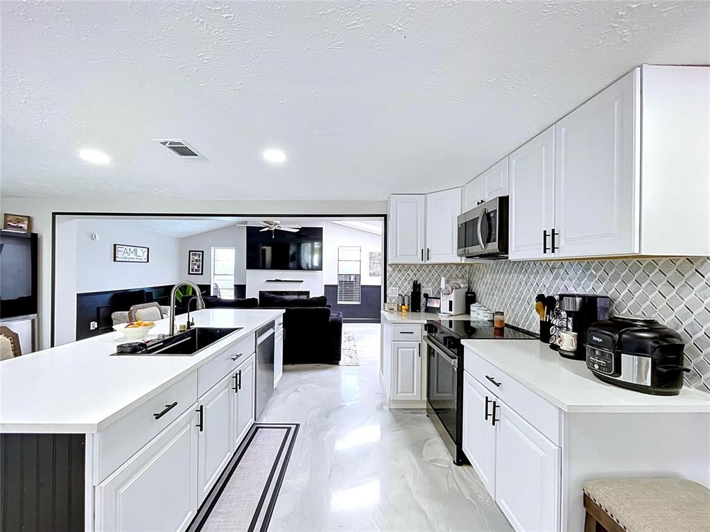 A modern kitchen features white cabinets, a large island with a sink, and stainless appliances — 6950 SOUTHWIND DRIVE, HUDSON, FL