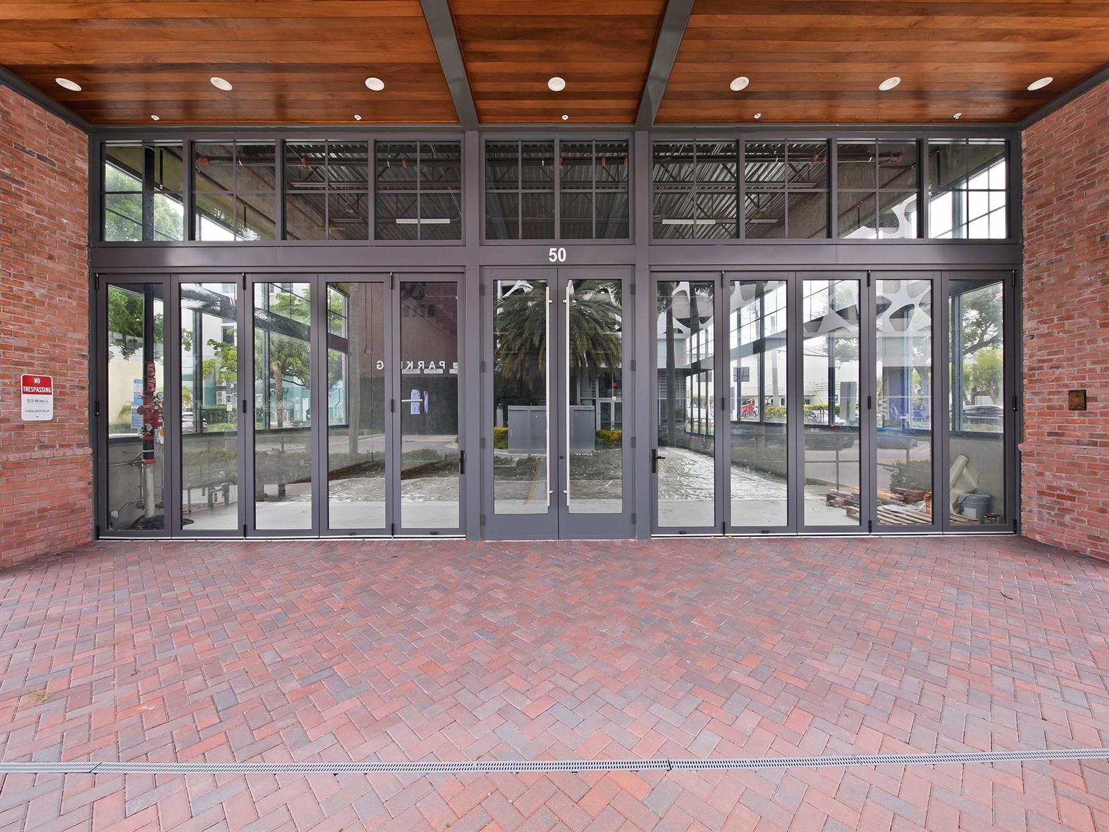The exterior entrance features a brick walkway leading to a glass-paneled folding door system — 50 SE 4th Avenue, Delray Beach FL 33483, DELRAY BEACH, FL