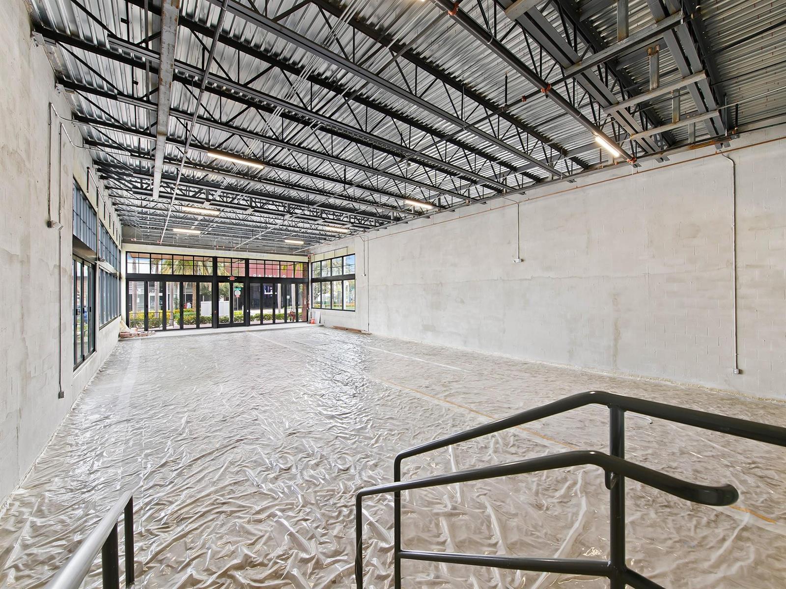 An empty commercial space features exposed metal ceiling trusses, concrete walls, and plastic-covered flooring — 50 SE 4th Avenue, Delray Beach FL 33483, DELRAY BEACH, FL
