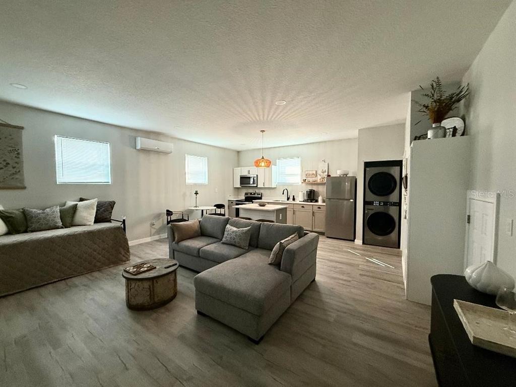 An open-concept living room and kitchen area with light wood flooring and gray furniture — 1183 CHESTNUT STREET UNIT B, CLERMONT, FL