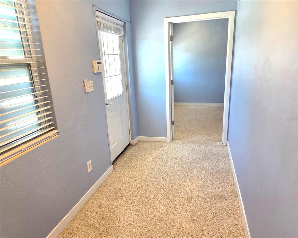 A small room with blue walls, a white door, and speckled flooring leads to another room — 921 RIDGEWOOD AVENUE UNIT A, HOLLY HILL, FL