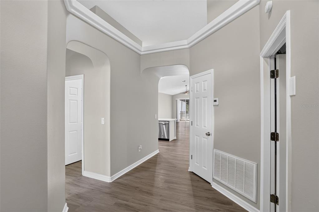 A hallway with light gray walls, crown molding, and wood-look flooring leads to a kitchen — 1844 MORNING STAR DRIVE, CLERMONT, FL