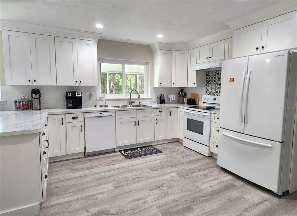 A white kitchen features shaker-style cabinets, marble-look countertops, stainless steel appliances, and wood-look flooring — 24595 NE HIGHWAY 315, FORT MC COY, FL