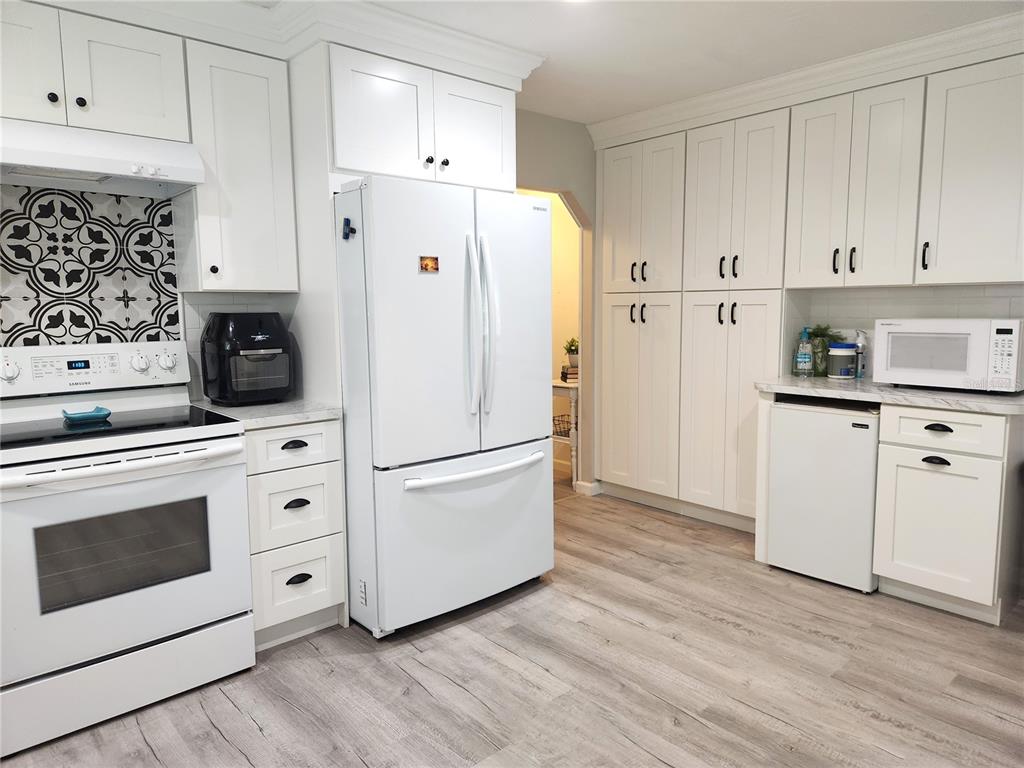 A kitchen features white cabinetry, stainless steel appliances, a patterned backsplash, and wood-look flooring — 24595 NE HIGHWAY 315, FORT MC COY, FL