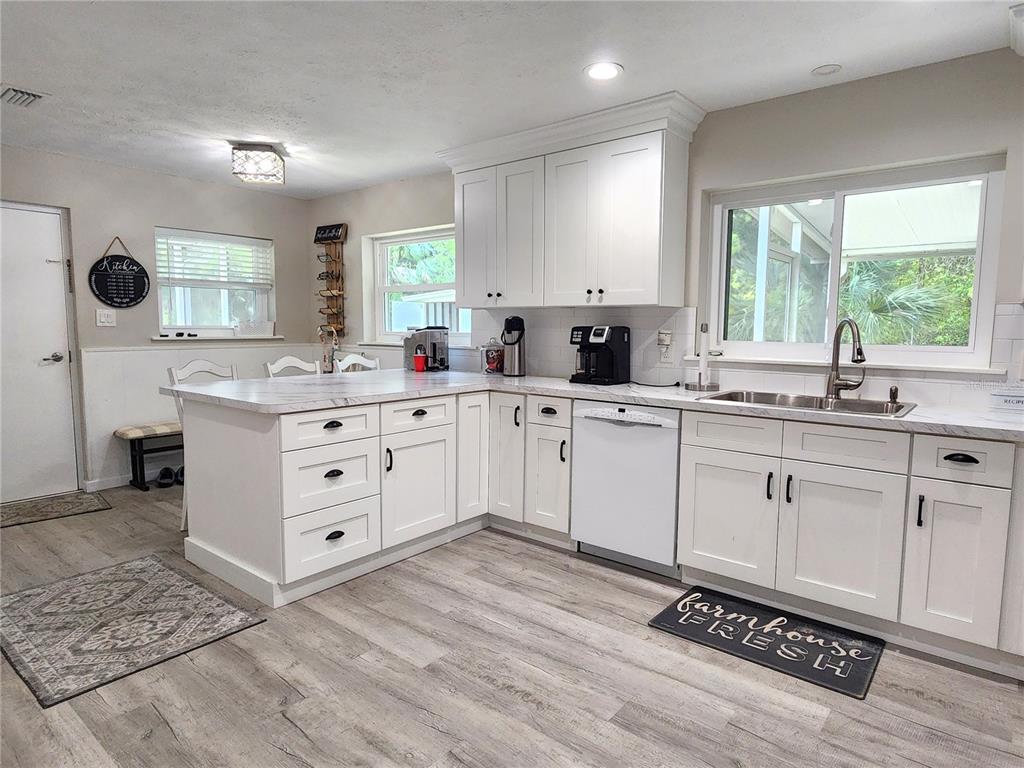 A kitchen features white cabinets, marble-look countertops, stainless steel appliances, and light wood-look flooring — 24595 NE HIGHWAY 315, FORT MC COY, FL