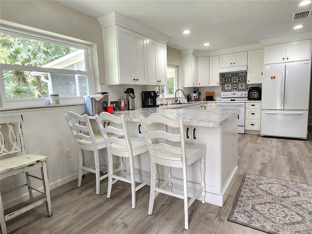 A white kitchen features a marble-topped island with three chairs and light wood flooring — 24595 NE HIGHWAY 315, FORT MC COY, FL