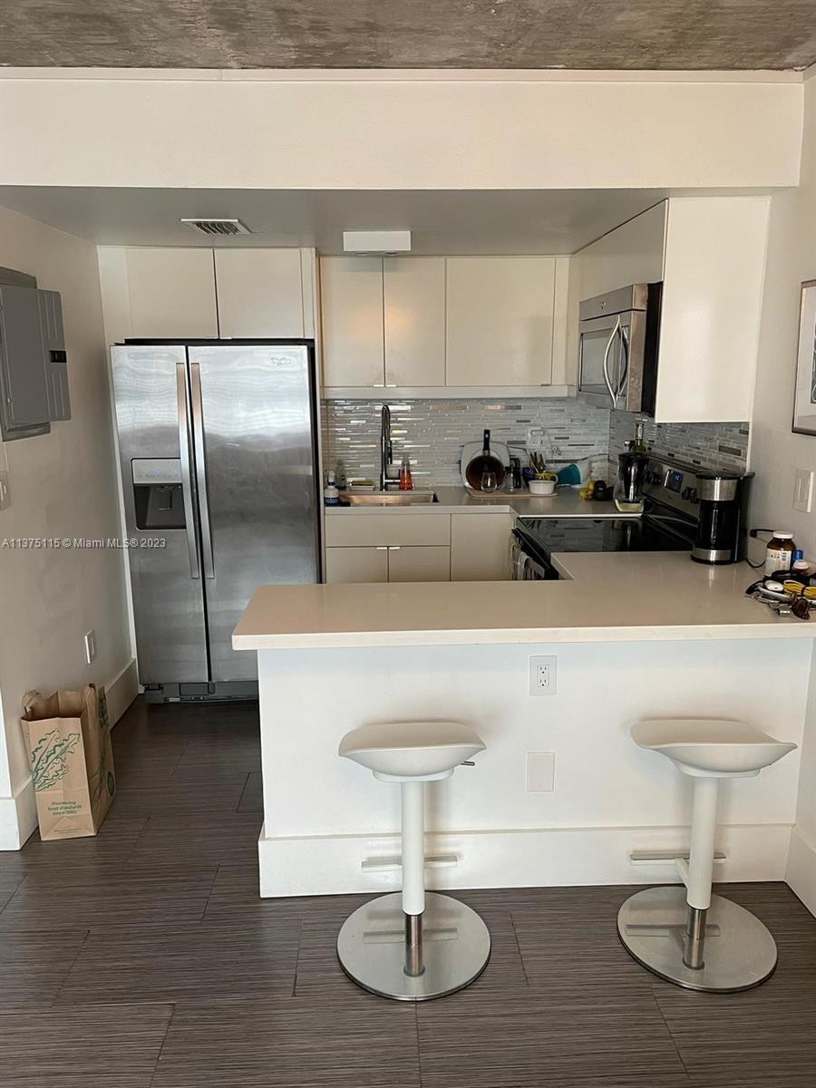 A kitchen features white cabinets, stainless steel appliances, a breakfast bar with stools, and tile flooring — 753 Michigan Ave # 2E, Miami Beach FL 33139, MIAMI BEACH, FL