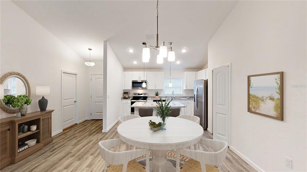 A dining area with a round table and chairs opens into a kitchen with white cabinets — 2816 TRICO ROAD, NORTH PORT, FL