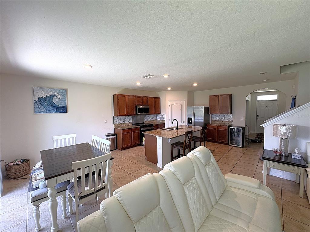 An open-concept kitchen and dining area features wood cabinets, granite countertops, and tile flooring — 1116 FOX PATH ROAD, DAVENPORT, FL