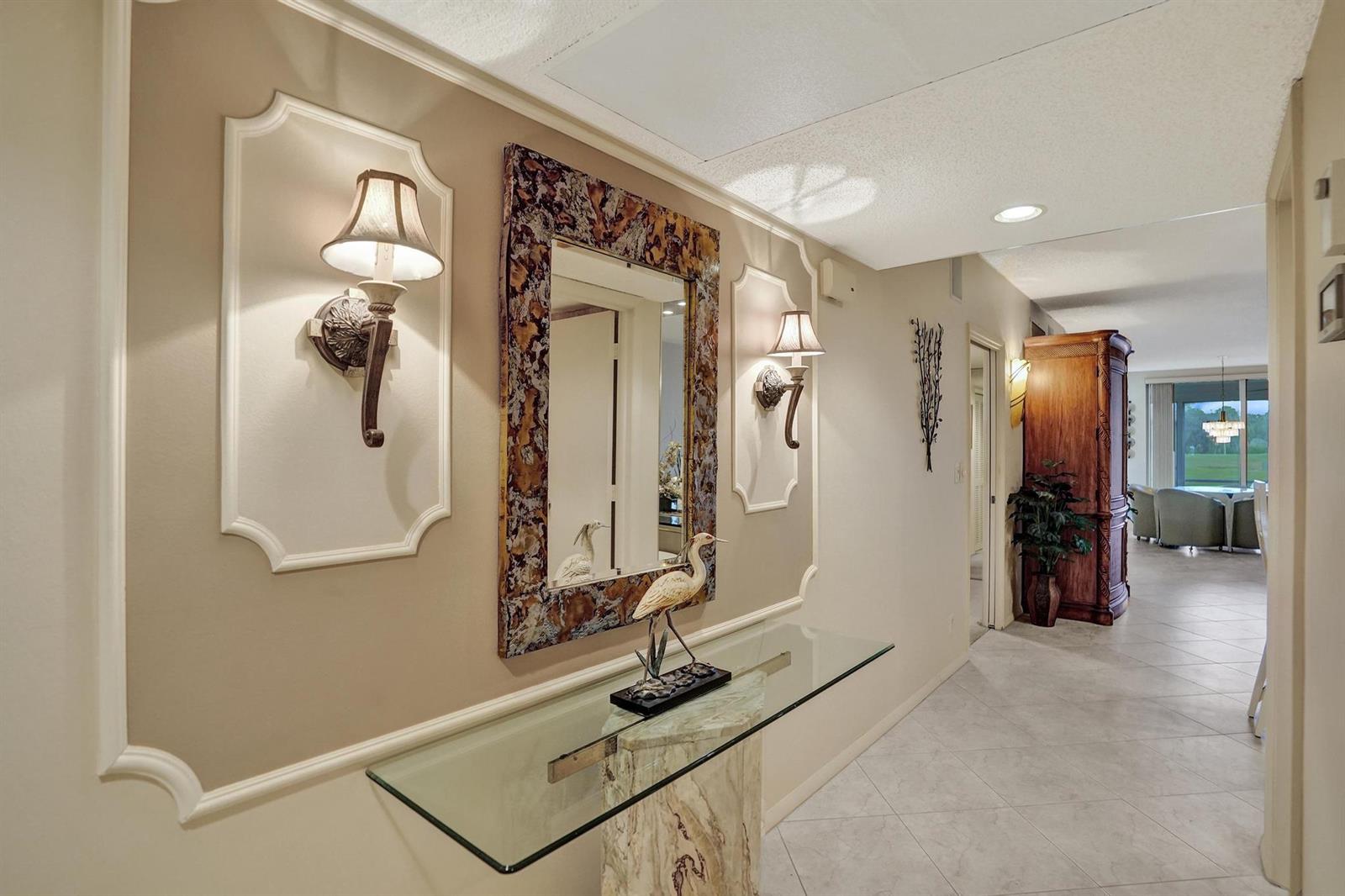 A hallway features a glass console table, a decorative mirror, and wall sconces on molding — 806 Cypress Boulevard # 104, Pompano Beach FL 33069, POMPANO BEACH, FL