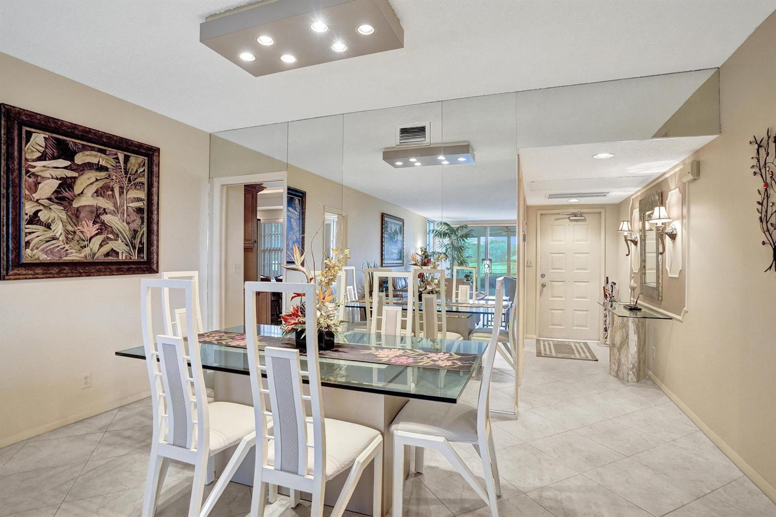 A dining room with a glass table, white chairs, tiled floors, and a mirrored wall — 806 Cypress Boulevard # 104, Pompano Beach FL 33069, POMPANO BEACH, FL