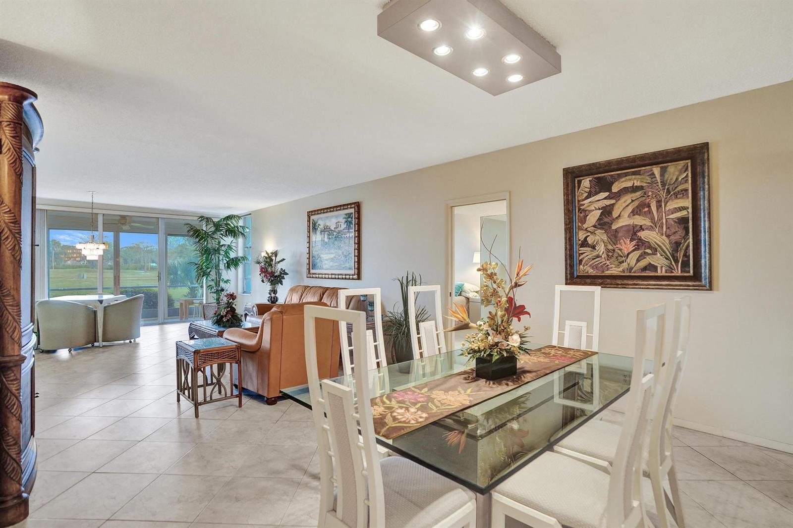 A dining area with a glass table and white chairs opens into a living room — 806 Cypress Boulevard # 104, Pompano Beach FL 33069, POMPANO BEACH, FL