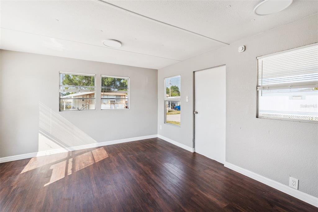 An empty room with gray walls, dark wood-look flooring, and multiple windows with blinds — 2854 LAKE ALFRED UNIT 6, WINTER HAVEN, FL
