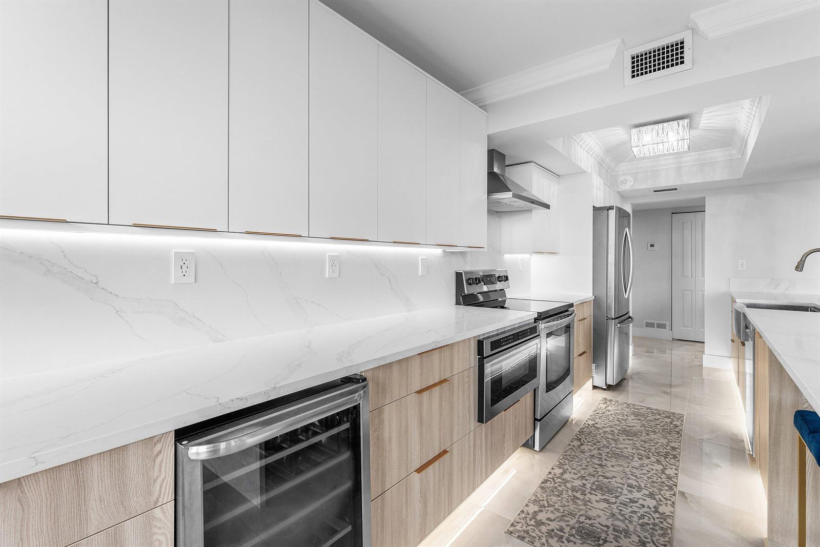A modern kitchen features white upper cabinets, light wood lower cabinets, and marble-patterned countertops — 5480 N Ocean Drive, Singer Island FL 33404, SINGER ISLAND, FL