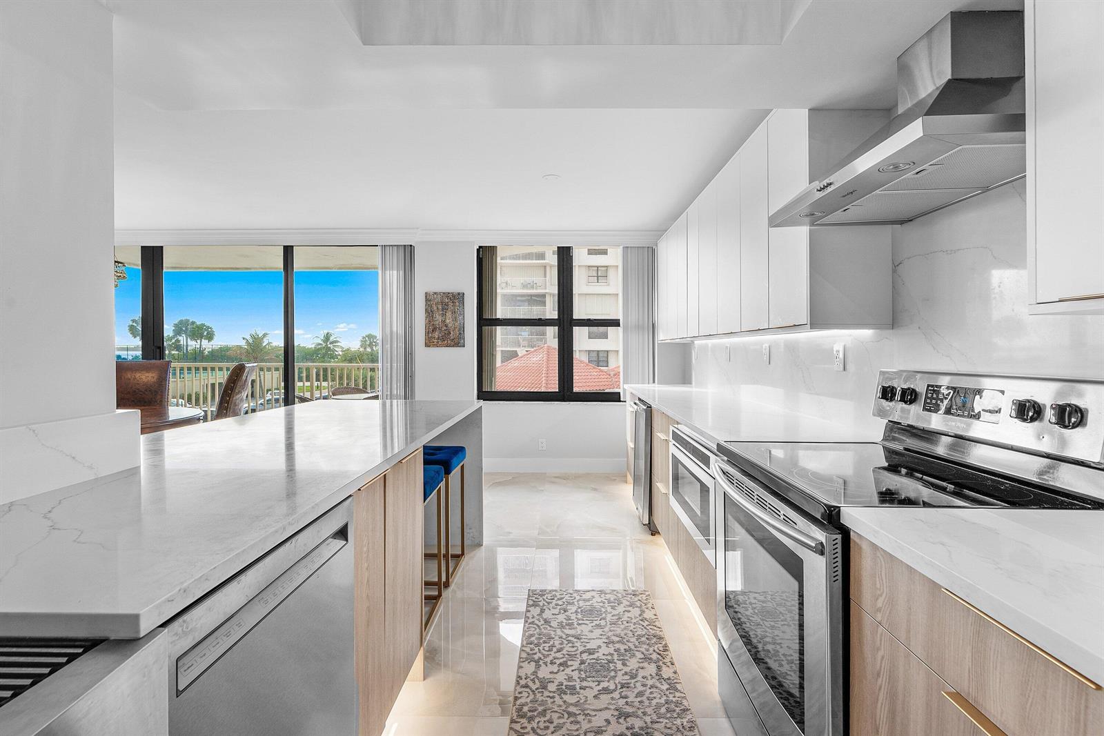 A modern kitchen features white cabinets, light wood accents, marble countertops, and a view of palm trees — 5480 N Ocean Drive, Singer Island FL 33404, SINGER ISLAND, FL