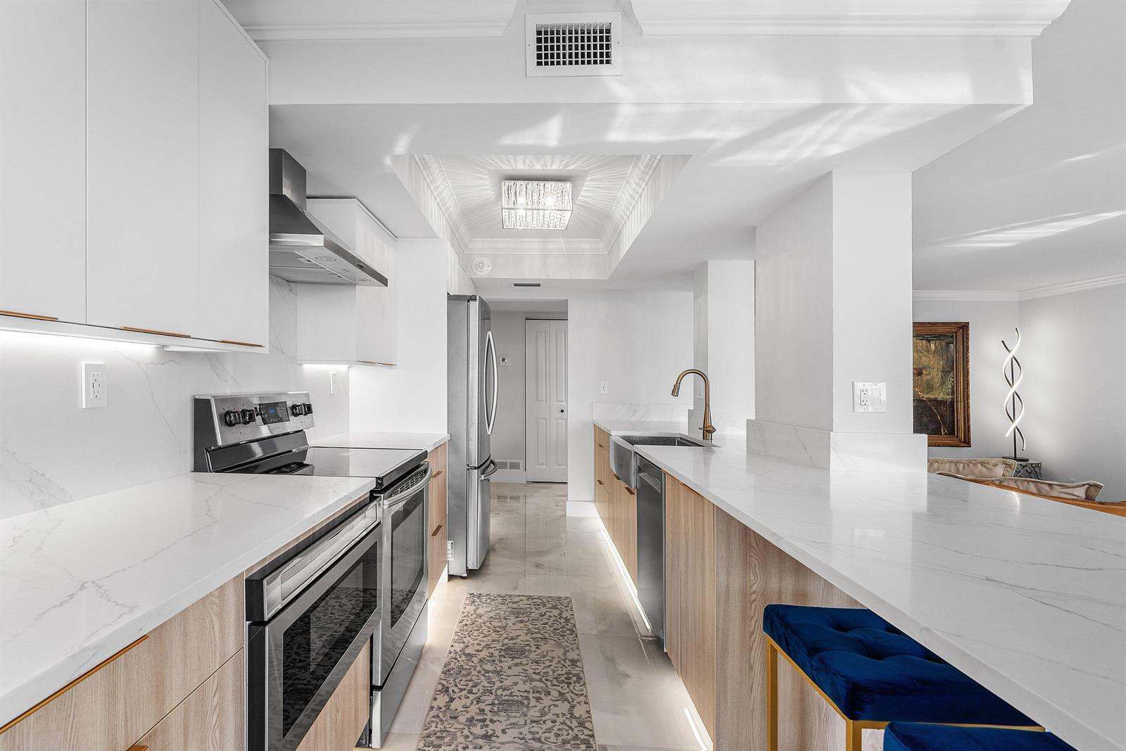 A modern kitchen features light wood cabinets, white marble countertops, and a blue velvet stool — 5480 N Ocean Drive, Singer Island FL 33404, SINGER ISLAND, FL