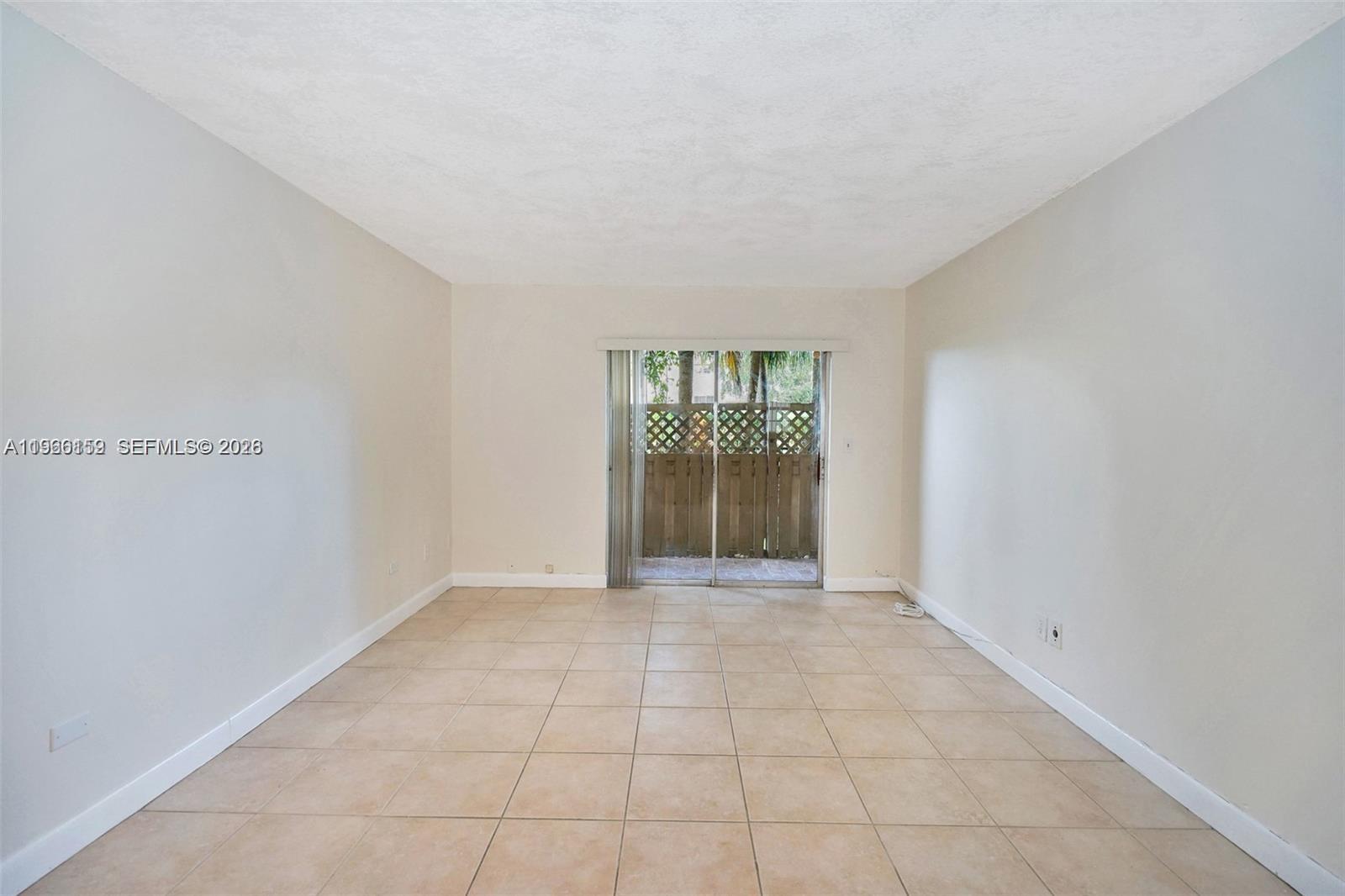 An empty room features beige tile flooring, light-colored walls, and a sliding glass door — 8500 SW 109 Ave # 102, Miami FL 33173, MIAMI, FL