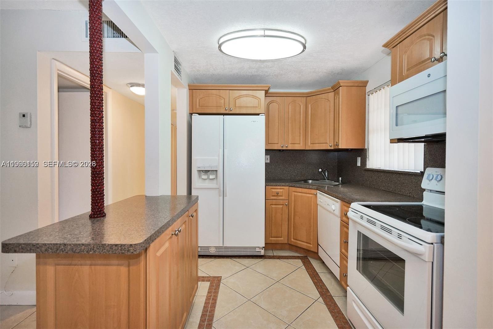 A kitchen features light wood cabinets, white appliances, and a dark speckled countertop — 8500 SW 109 Ave # 102, Miami FL 33173, MIAMI, FL