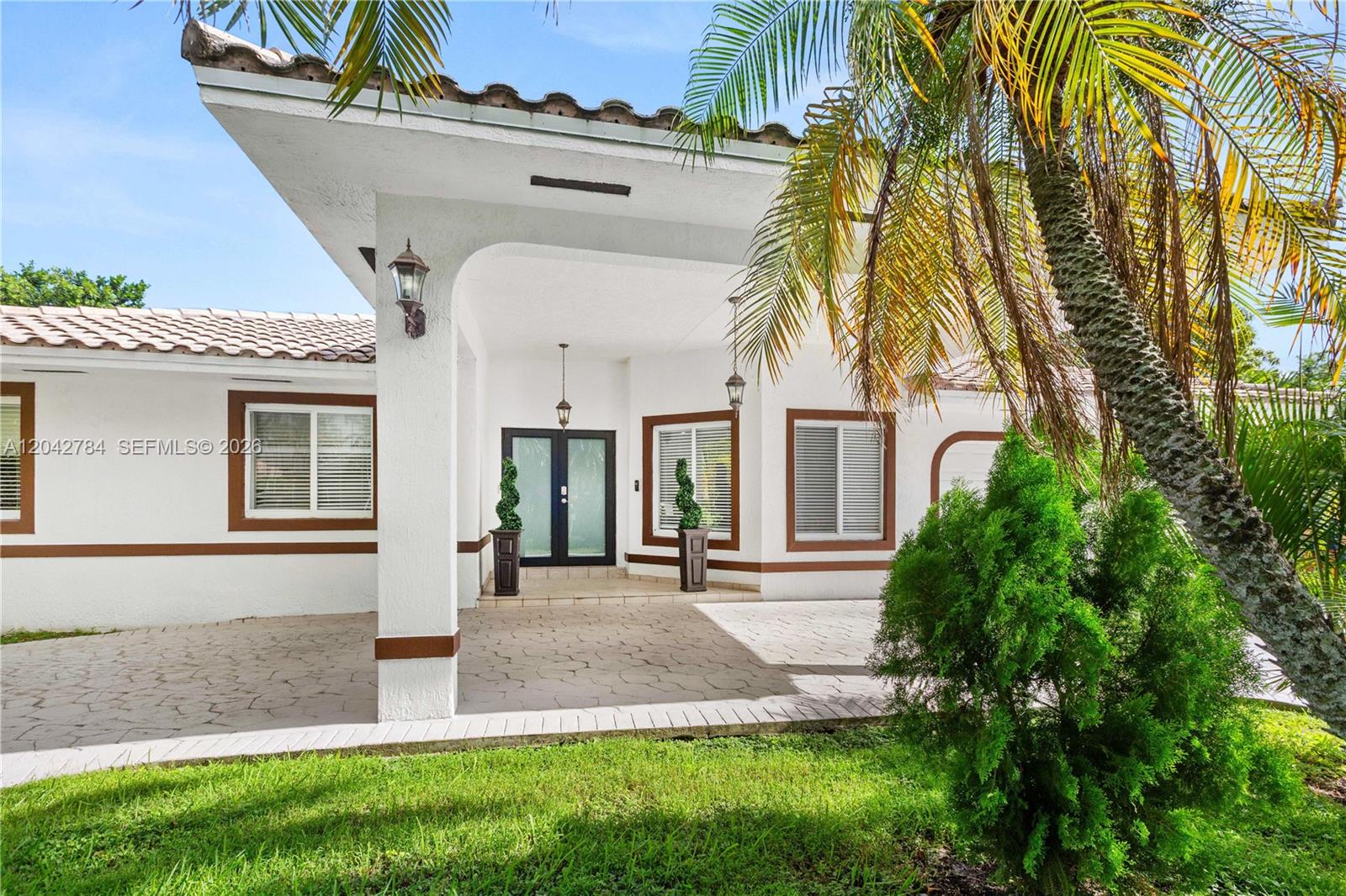 The exterior of a white house features a covered entryway, brown trim, and palm trees — 9840 NW 28th Ter, Doral FL 33172, DORAL, FL