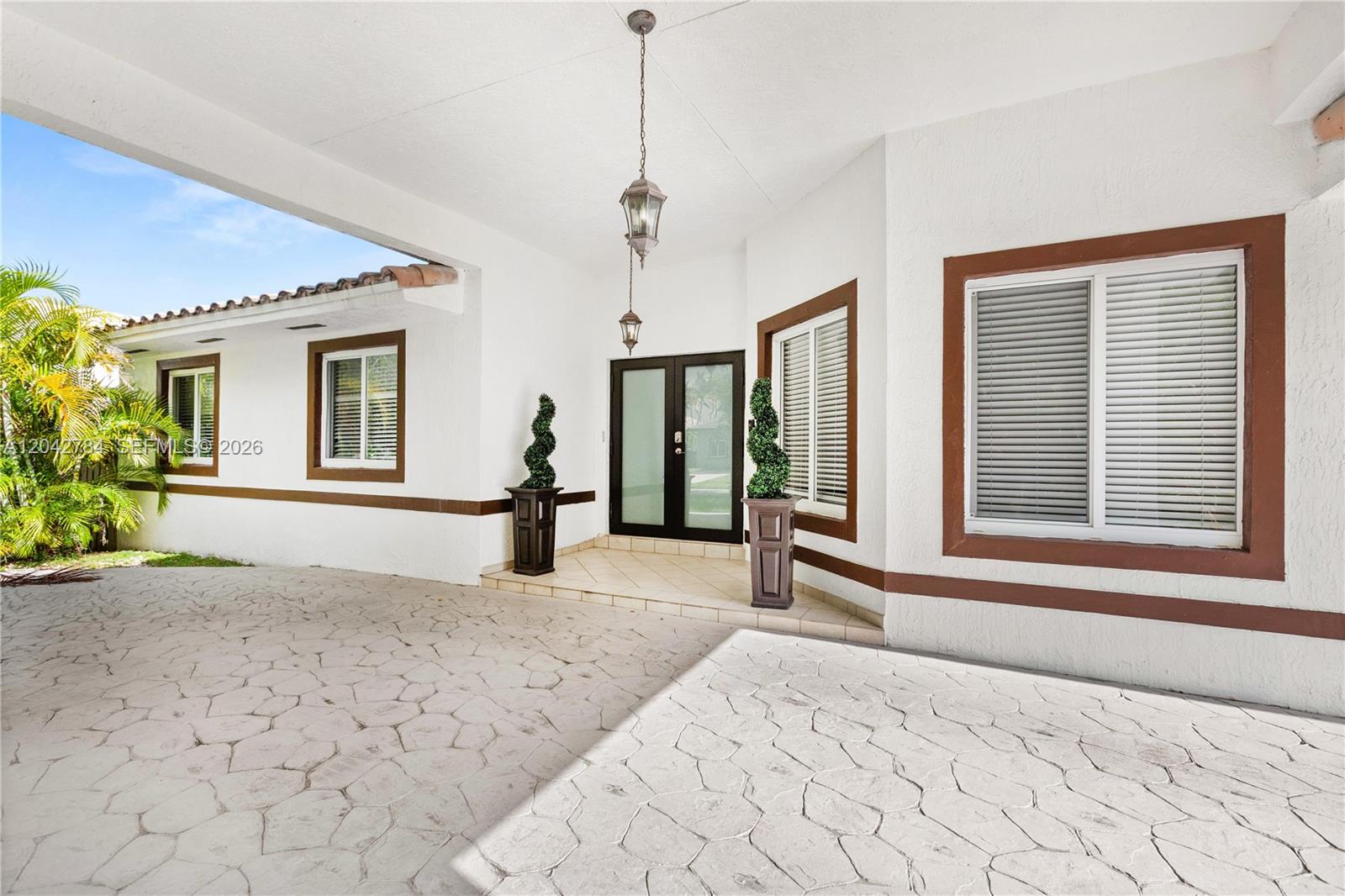 A covered entryway features a stone-paved driveway, white stucco walls, brown trim, and double doors — 9840 NW 28th Ter, Doral FL 33172, DORAL, FL