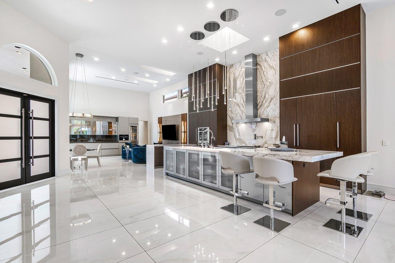 A modern kitchen features a large marble island, dark wood cabinetry, and white tile flooring — 3506 NW Clubside Circle, Boca Raton FL 33496, BOCA RATON, FL