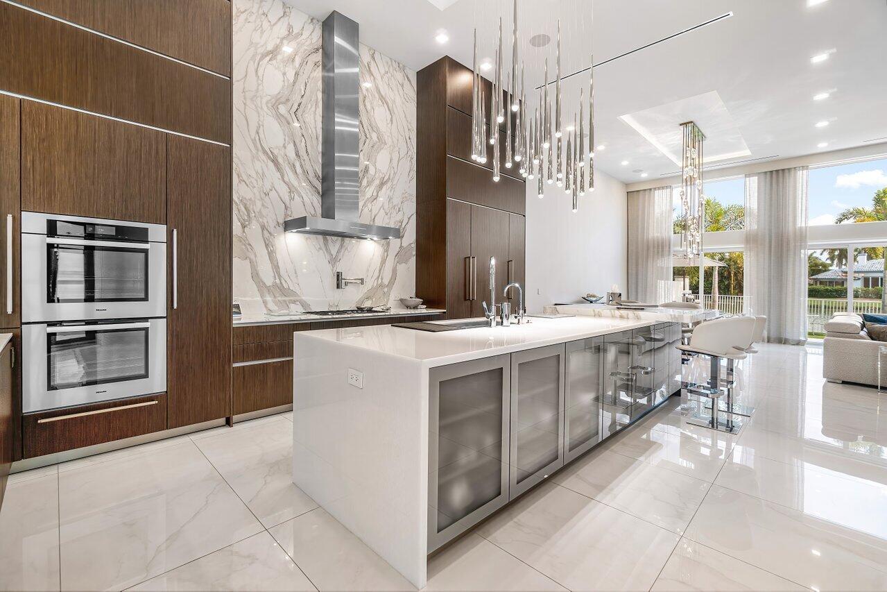 A modern kitchen features dark wood cabinetry, a marble backsplash, and a large white island — 3506 NW Clubside Circle, Boca Raton FL 33496, BOCA RATON, FL