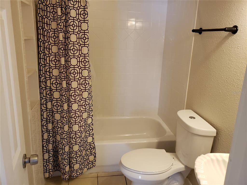 A bathroom features a white bathtub with a patterned shower curtain, a toilet, and a sink — 134 LAGO VISTA BOULEVARD, CASSELBERRY, FL