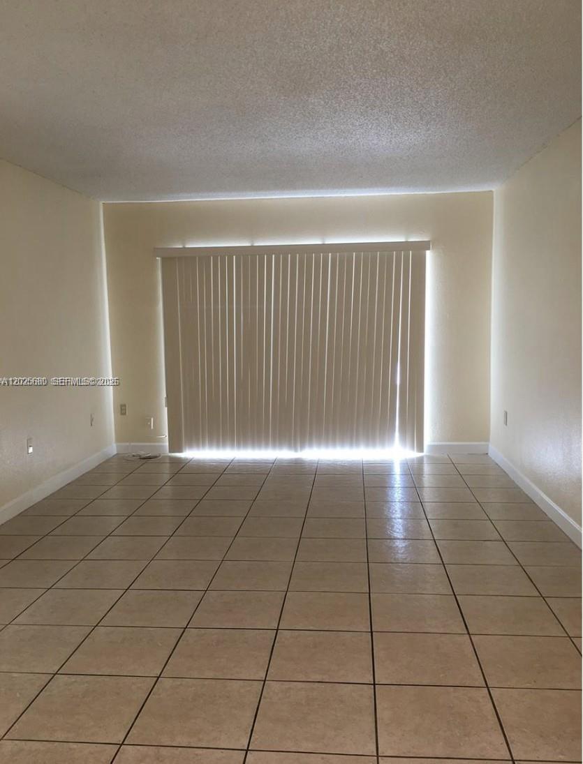 An empty living room features beige tile flooring, white walls, and a sliding glass door — 10900 SW 104th St # 210, Miami FL 33176, MIAMI, FL