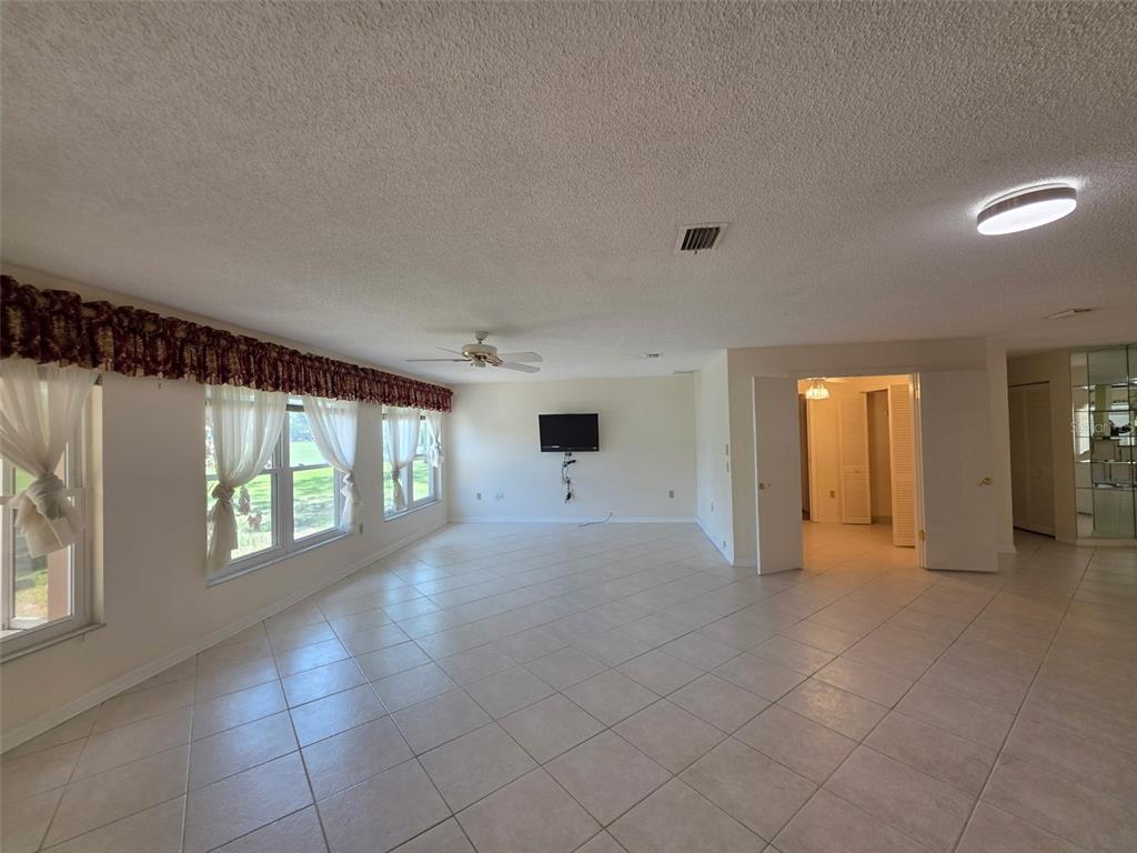 A spacious living room features light tile flooring, a ceiling fan, and large windows — 2376 BENT PINE COURT, SPRING HILL, FL
