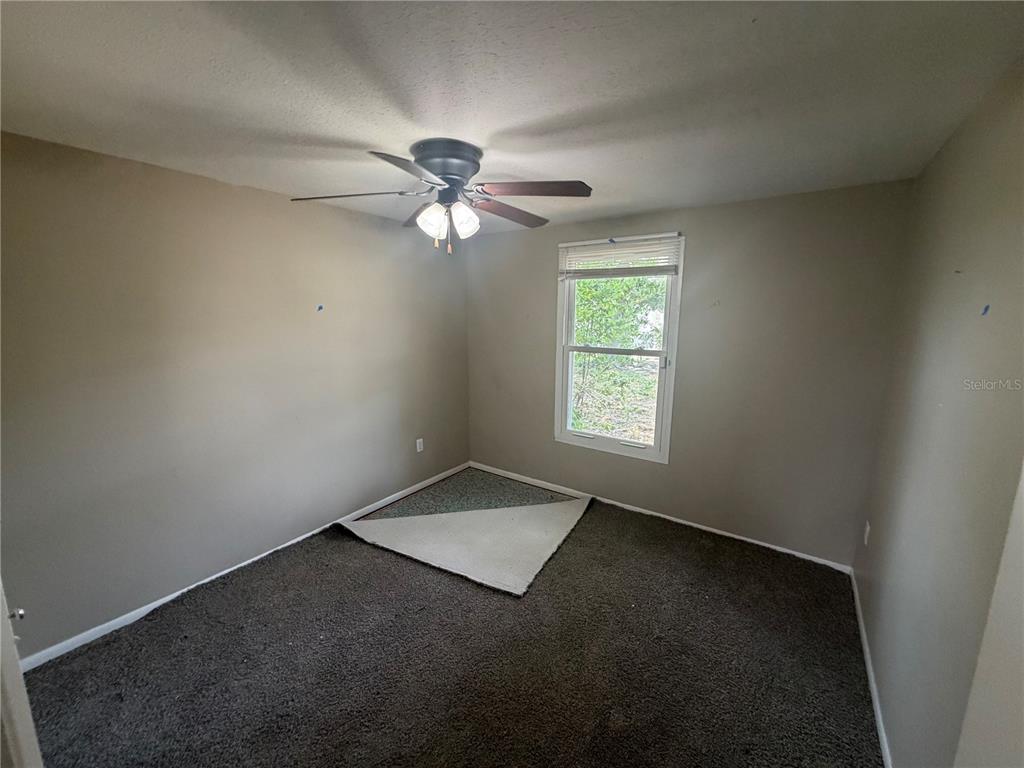 An empty bedroom features gray walls, a ceiling fan, and dark carpet with a patch — 2129 DANA PLACE, LAKELAND, FL