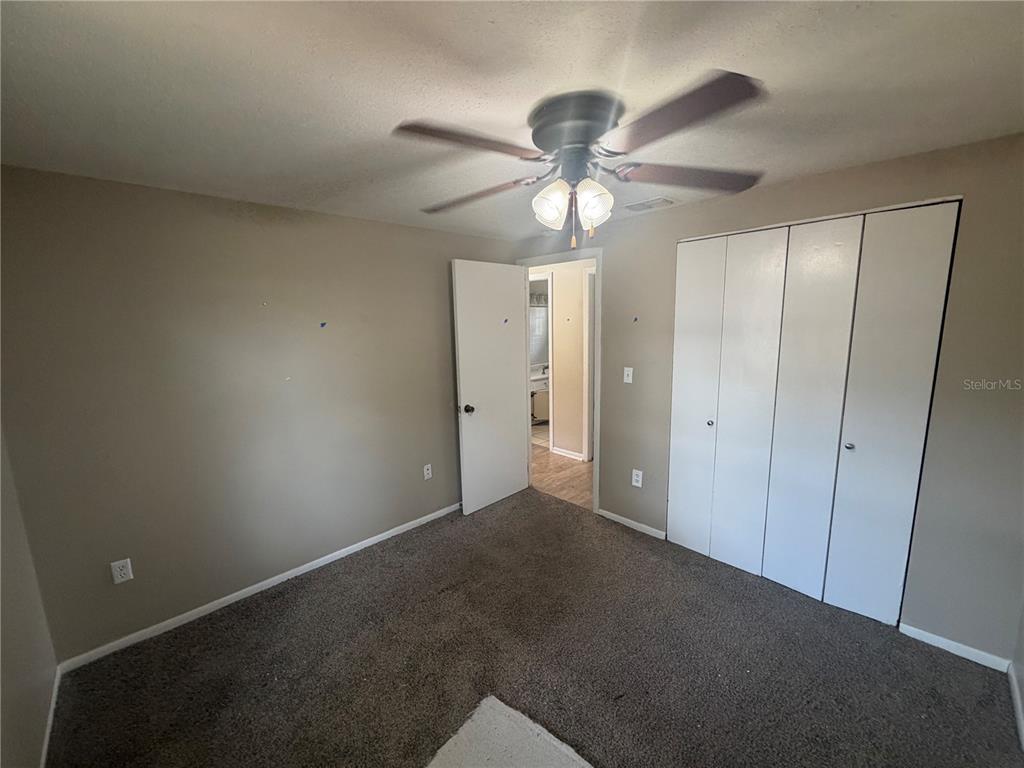 A bedroom with gray carpet, beige walls, a ceiling fan, and white closet doors — 2129 DANA PLACE, LAKELAND, FL