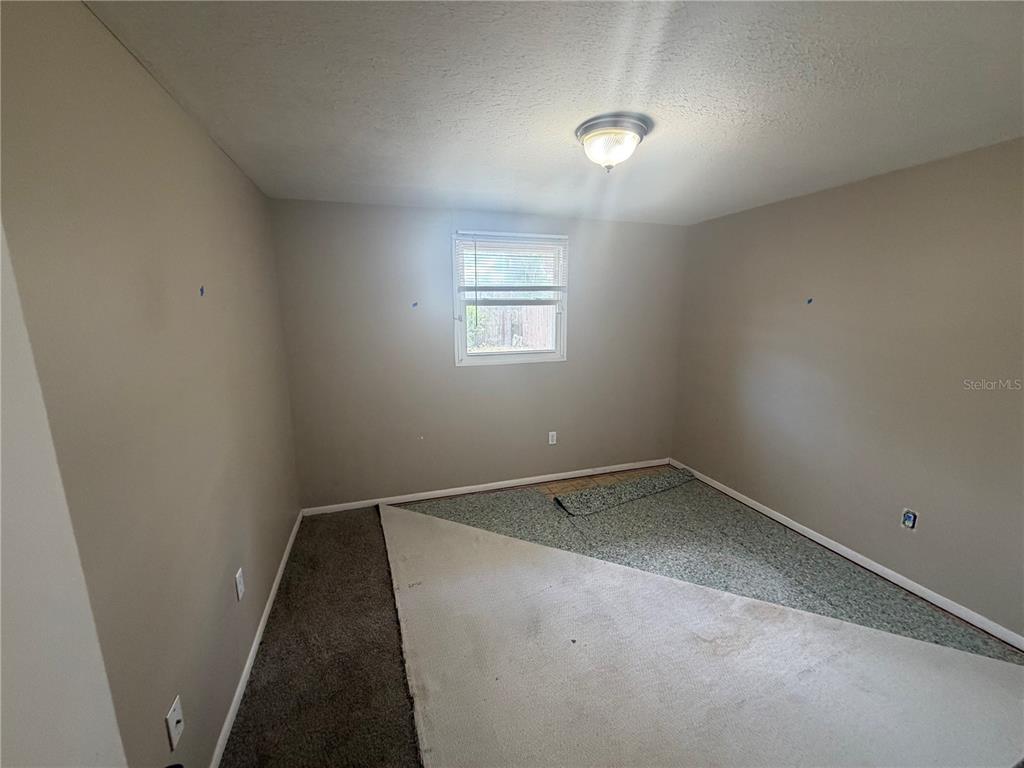 An empty bedroom features beige walls, a ceiling light, and partially removed carpet flooring — 2129 DANA PLACE, LAKELAND, FL