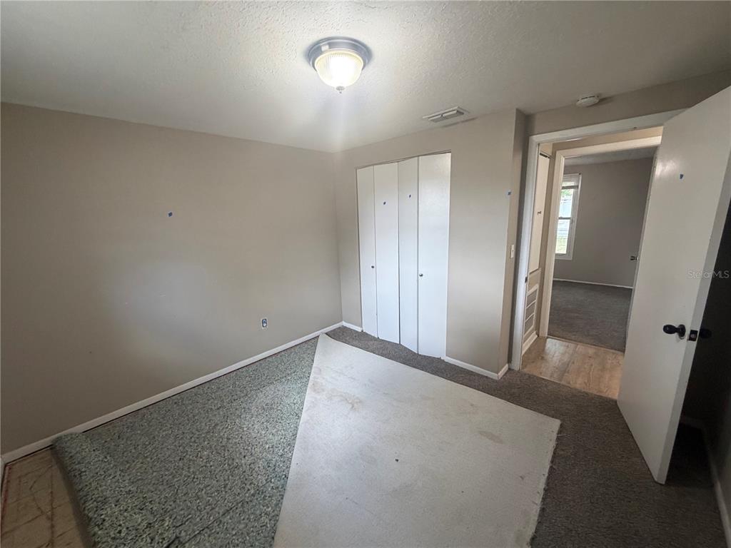An empty bedroom features beige walls, a white closet, and partially installed gray carpeting — 2129 DANA PLACE, LAKELAND, FL
