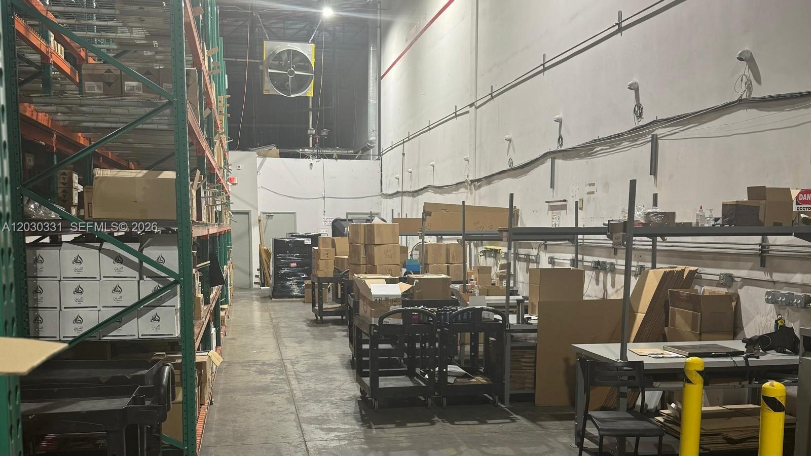 A warehouse interior features metal storage racking, cardboard boxes, and a large ceiling-mounted fan — 10133 USA TODAY WAY, Miramar FL 33025, MIRAMAR, FL