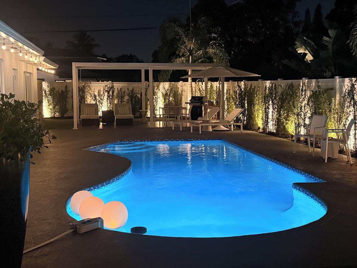 A backyard swimming pool at night with illuminated floating spheres and surrounding patio furniture — 541 Ibis Drive, Delray Beach FL 33444, DELRAY BEACH, FL