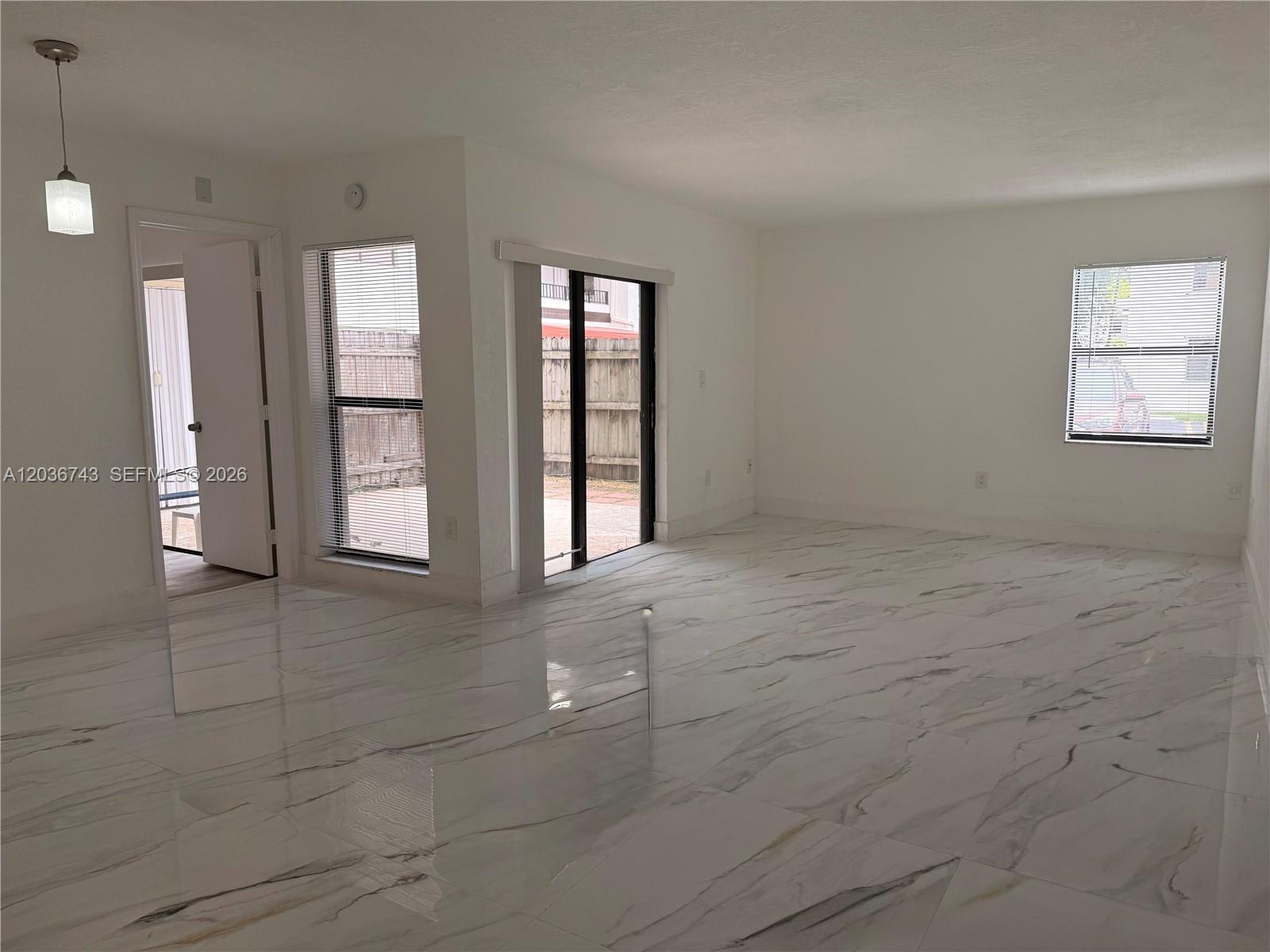 An empty room features white walls, marble-look tile flooring, a sliding glass door, and windows — 10875 NW 7th St # 36, Miami FL 33172, MIAMI, FL