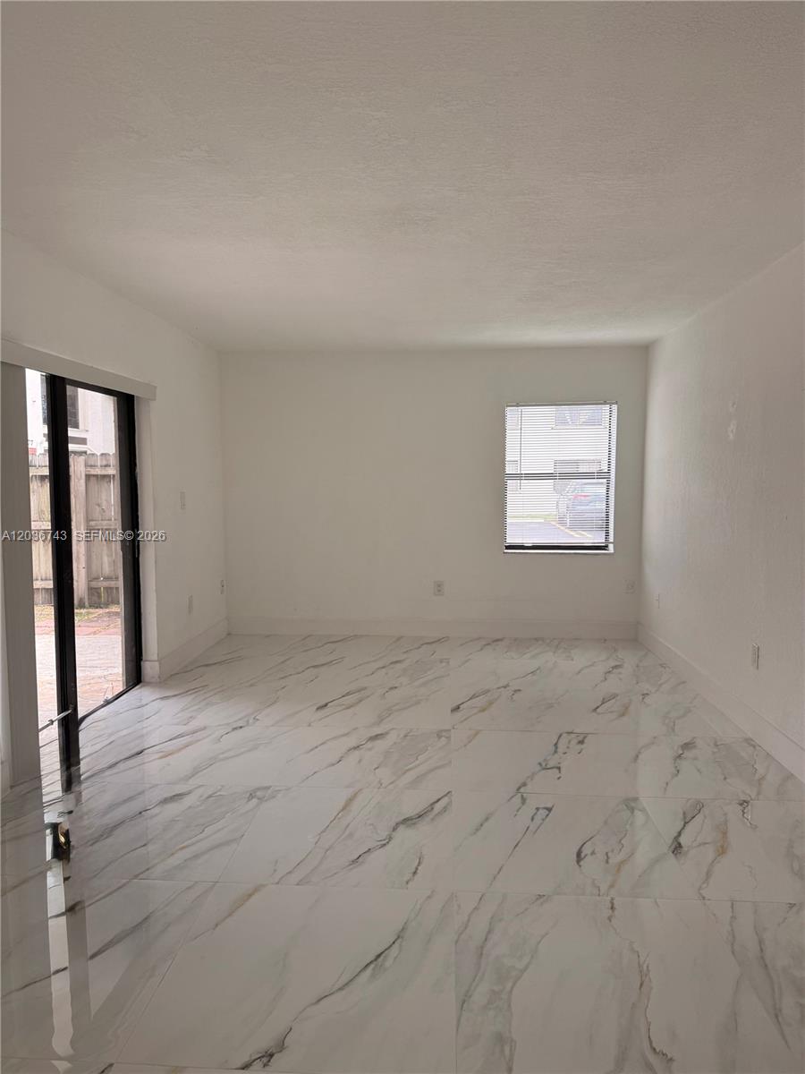 An empty room features white marble-look tile flooring, a sliding glass door, and one window — 10875 NW 7th St # 36, Miami FL 33172, MIAMI, FL