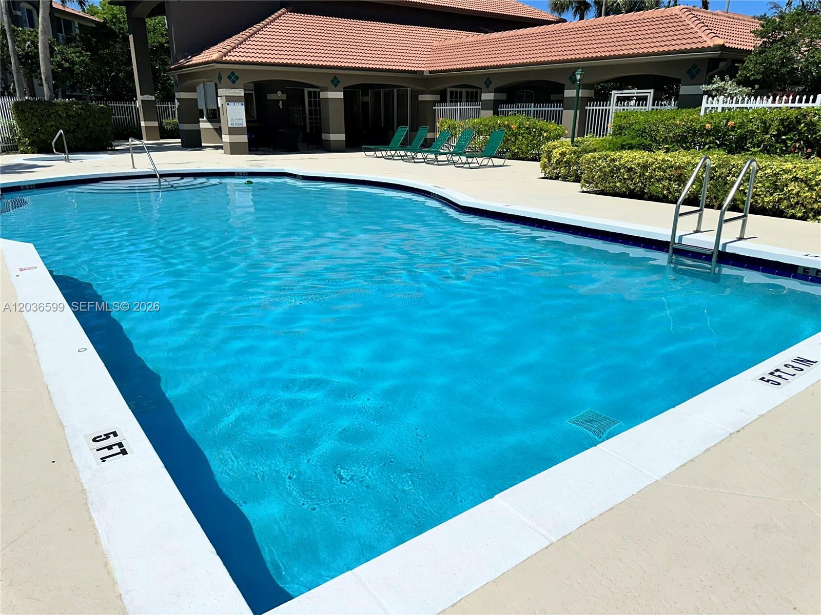 A rectangular swimming pool with a ladder and depth markers sits in front of a building — 460 S Park Rd # 203, Hollywood FL 33021, HOLLYWOOD, FL