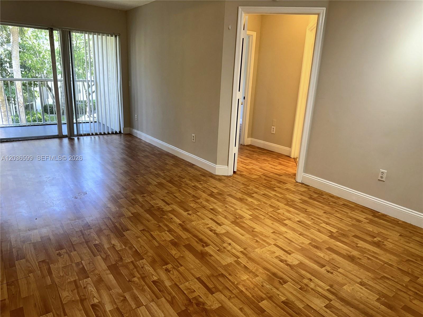 An empty room features wood-look flooring, beige walls, and a sliding glass door to a balcony — 460 S Park Rd # 203, Hollywood FL 33021, HOLLYWOOD, FL