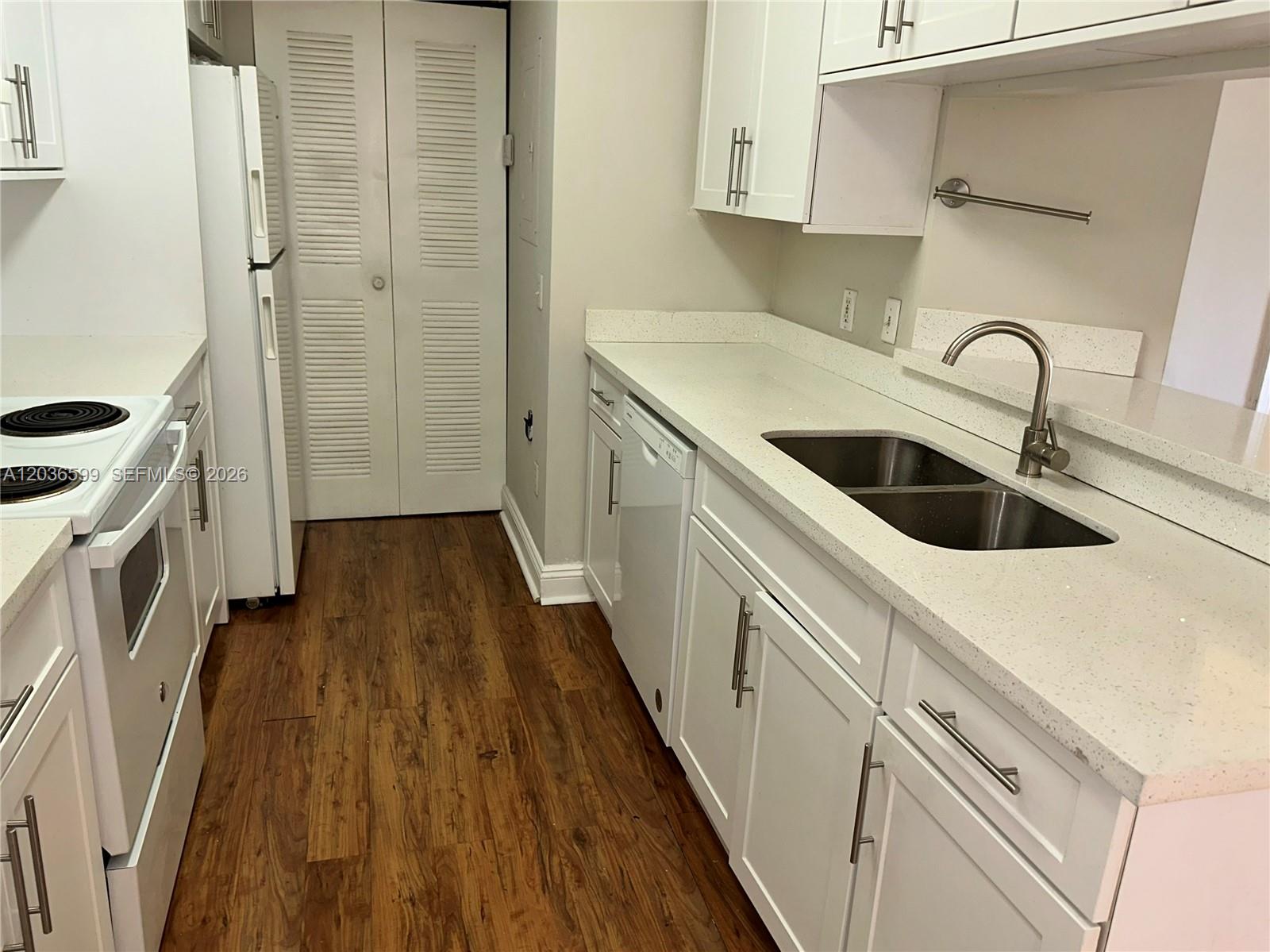 A kitchen features white cabinets, white appliances, a double sink, and wood-look flooring — 460 S Park Rd # 203, Hollywood FL 33021, HOLLYWOOD, FL