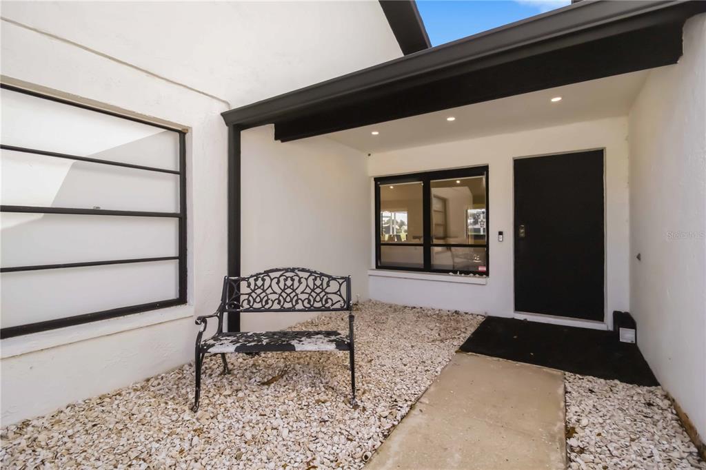 A covered entryway features white walls, a black door, a window, and a gravel floor — 4134 EASTWOOD DRIVE, SARASOTA, FL