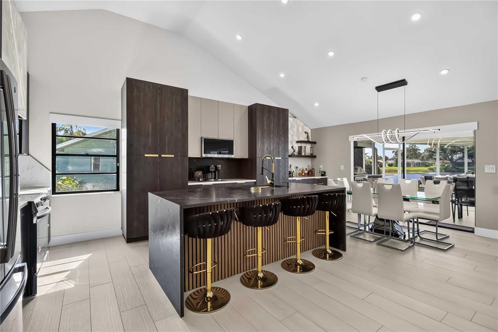 A modern kitchen features a dark marble island with gold stools and wood-slat detailing — 4134 EASTWOOD DRIVE, SARASOTA, FL